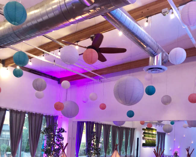 A spacious room is decorated with paper lanterns and features several illuminated teepees, with plush seating arranged on the floor.