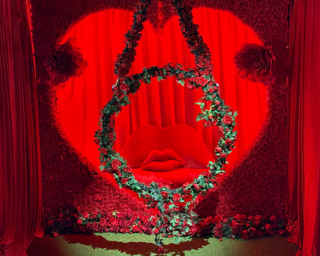 A floral arrangement in shades of red forms a heart shape with a swing adorned with greenery at the center.