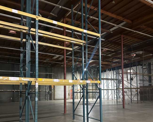 The image shows a spacious warehouse interior with metal shelving units and a concrete floor.