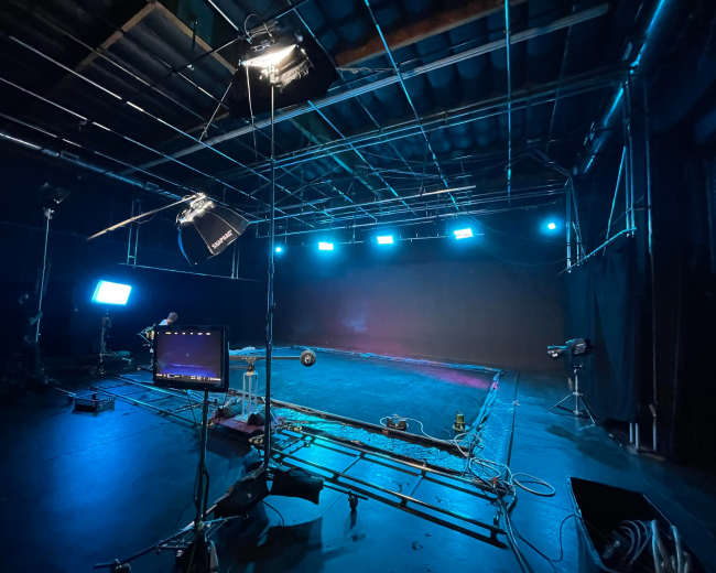 A dimly lit studio setup features various lights, cables, and a black backdrop.