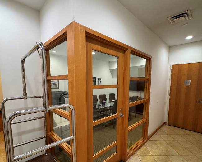 A small meeting room with glass windows is located at the corner of a hallway, and a cart is positioned nearby.