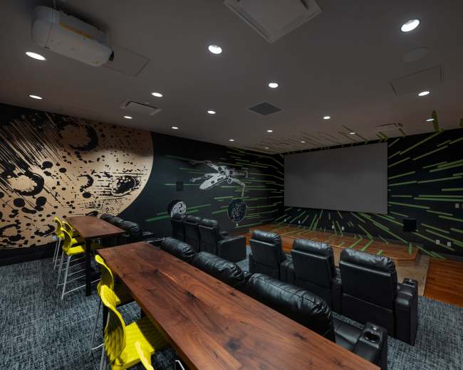 The image shows a modern home theater with a large projection screen, leather recliner seats, and a decorative wall featuring a space-themed mural.