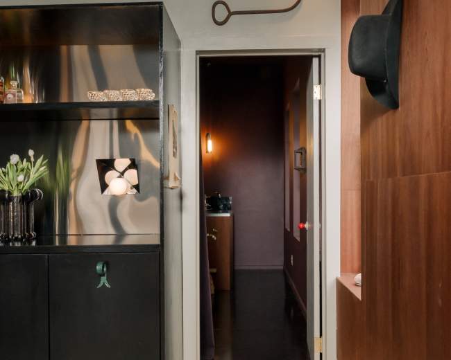 The image shows a hallway with a dark wooden wall on one side and a black storage unit on the other, leading to a door at the end.