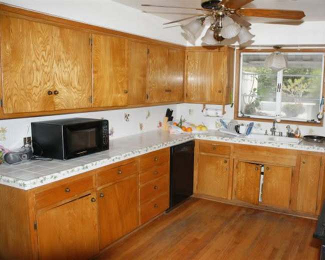 A kitchen features wooden cabinets, a microwave, and a window overlooking a small garden.