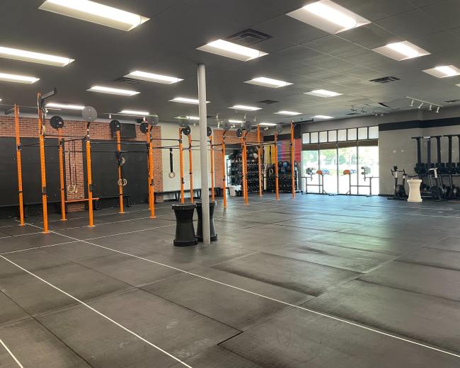 A spacious gym area with black flooring and several pull-up bars, gymnastic rings, and exercise equipment against the walls.