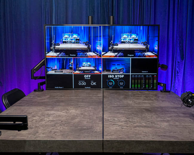 A modern control room setup features multiple screens displaying camera feeds and status indicators against a blue backdrop.