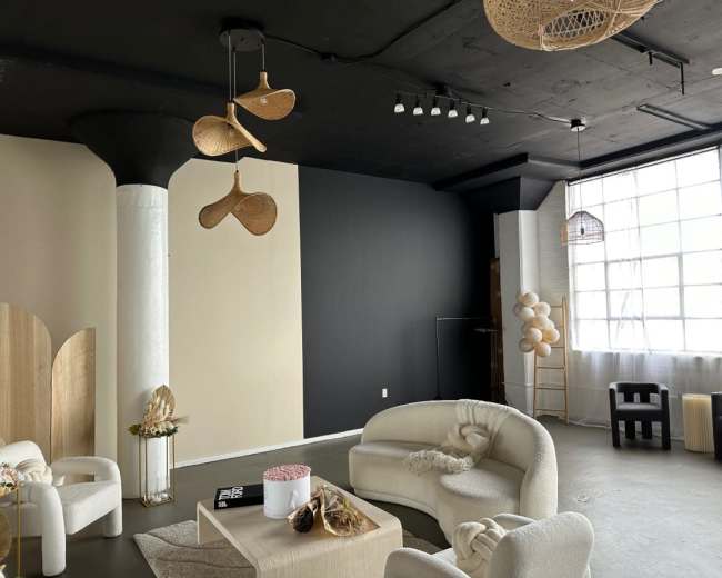 A modern interior space with beige and dark walls, featuring circular seating arrangements, decorative elements, and large windows allowing natural light.