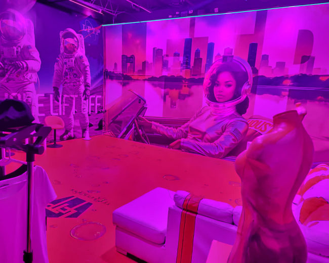 The room features vibrant pink walls adorned with large astronaut and space-themed murals, along with modern furniture and clothing on display.