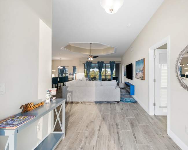 The interior of a modern living space features a foyer with a console table, leading to a light-filled open living area furnished with a sofa and entertainment center.