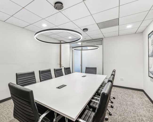 The image shows a modern conference room with a large white table surrounded by black leather chairs and two circular pendant lights hanging above.