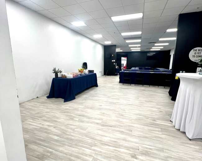 The image shows a spacious, well-lit room with a table set up for refreshments on the left and seating arranged in the background.