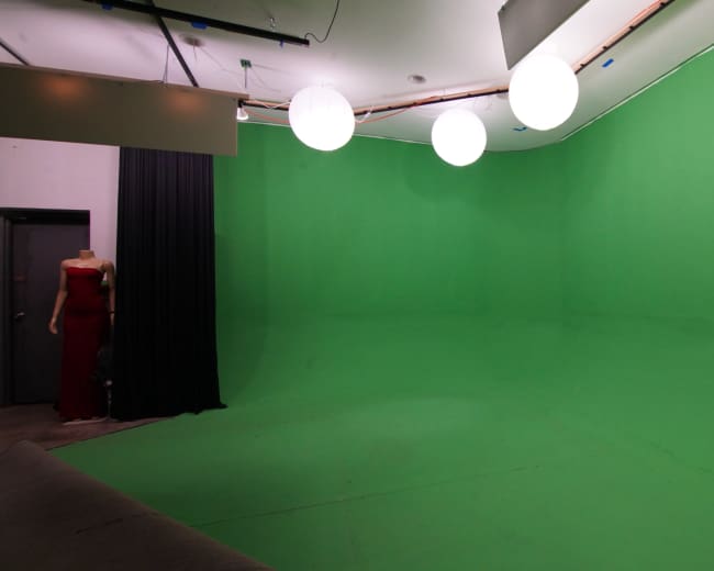 The image shows a green-screen studio with a seamless green backdrop and three hanging round lights.