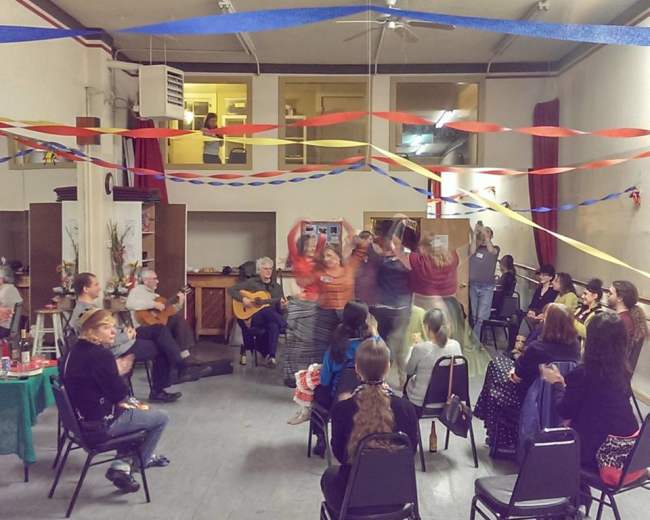 A group of people dance in a decorated room filled with colorful streamers while others sit and watch.
