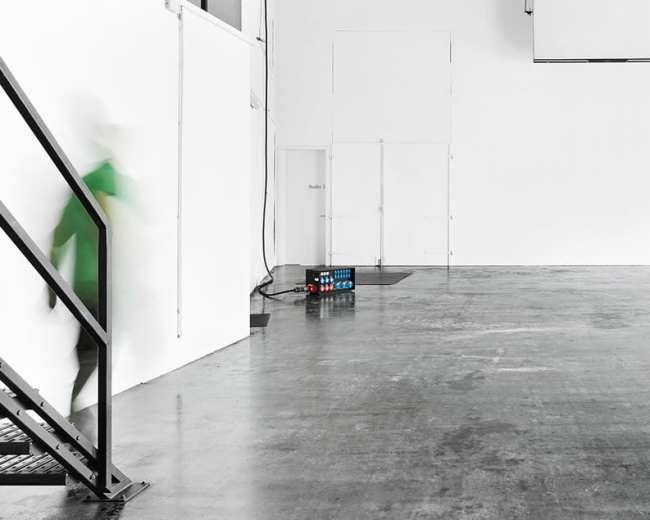 A person is walking down a staircase in an empty, brightly lit room with white walls and a concrete floor.