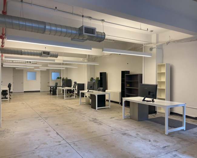 The image shows a spacious, modern office with several desks and computers arranged in an open layout.