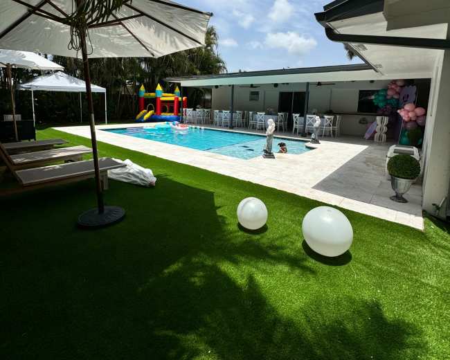 The image shows a sunny backyard with a swimming pool surrounded by lounge chairs, a bounce house, and decorative balloons.