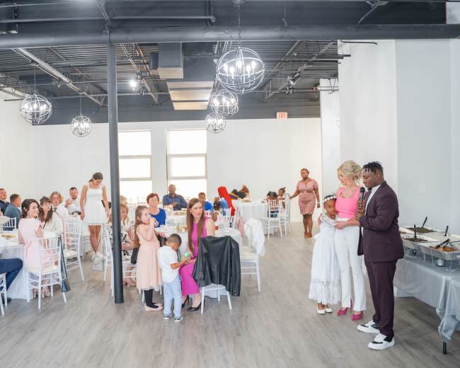 A diverse group of people gathers at a reception in a spacious, well-lit venue with white walls and modern decor.