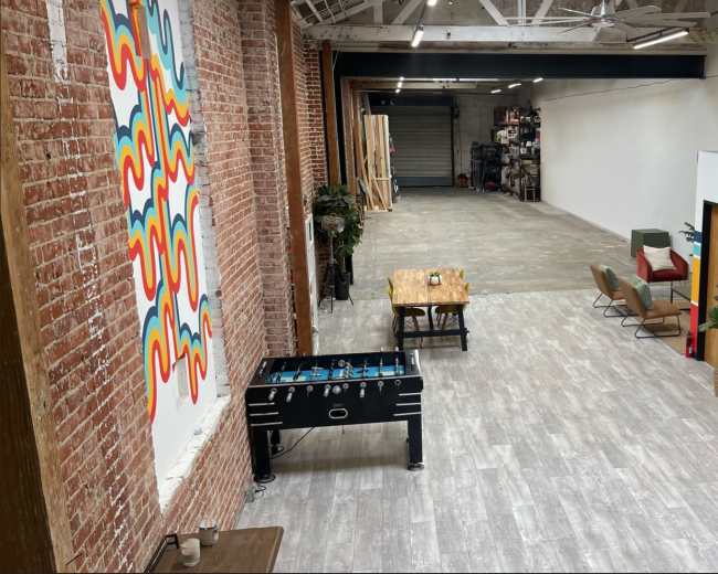 An open, spacious interior with exposed brick walls, a foosball table, a dining table, and a colorful retro refrigerator.