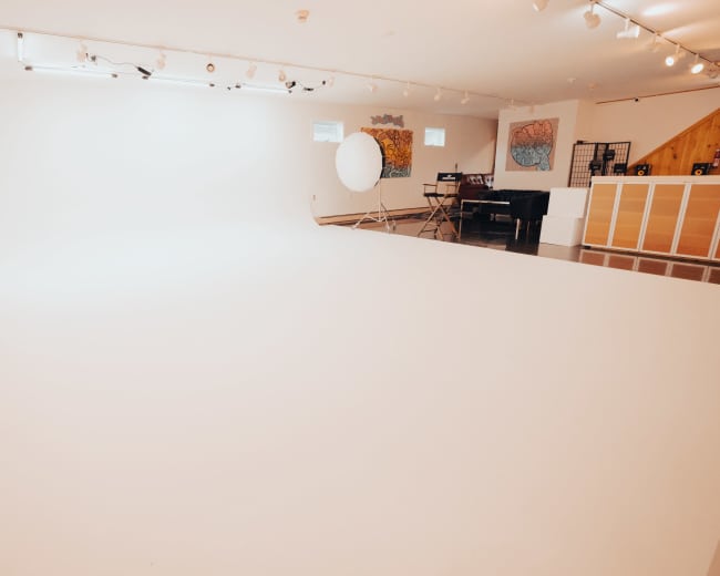 A spacious studio with a seamless white backdrop, soft lighting, and a few artistic decorations on the walls.