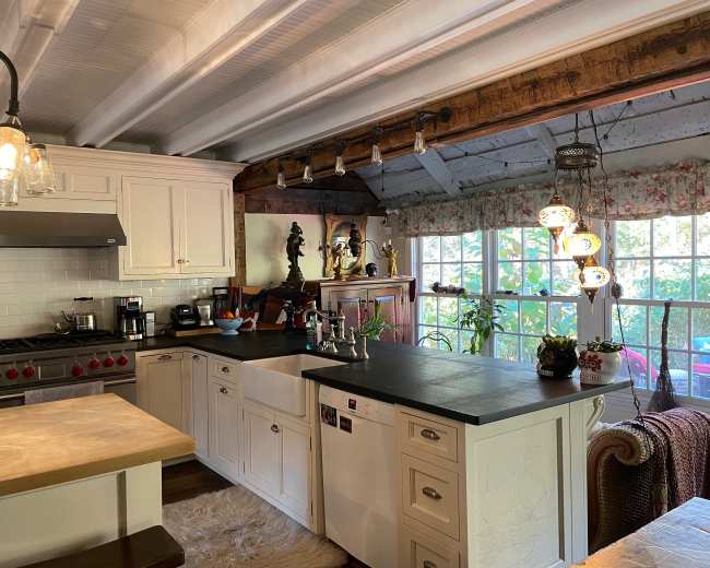 A modern kitchen with white cabinets, a large stove, and a countertop, featuring natural light from a window adorned with floral curtains.