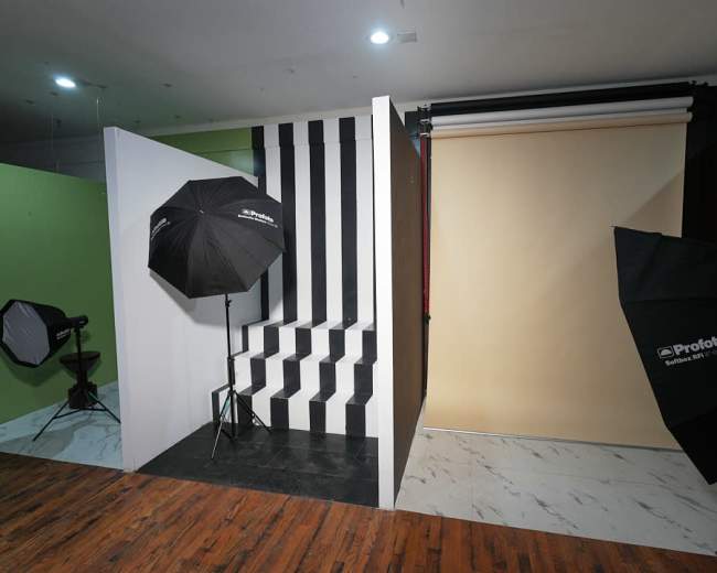 The image shows a photography studio setup with contrasting backdrops, lighting equipment, and a staircase.