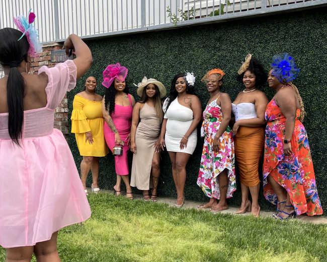 A group of women in colorful dresses poses for a photo in front of a green wall.