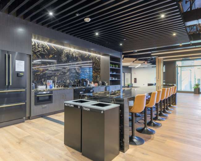 The image shows a modern kitchen with a black and gold marble backsplash, stainless steel appliances, and a large island with bar stools.