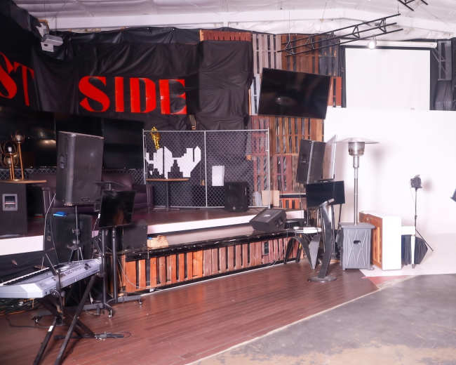 The image shows a well-lit photography studio featuring various equipment, including lighting setups, a blank backdrop, and a music keyboard against a backdrop of wooden panels.