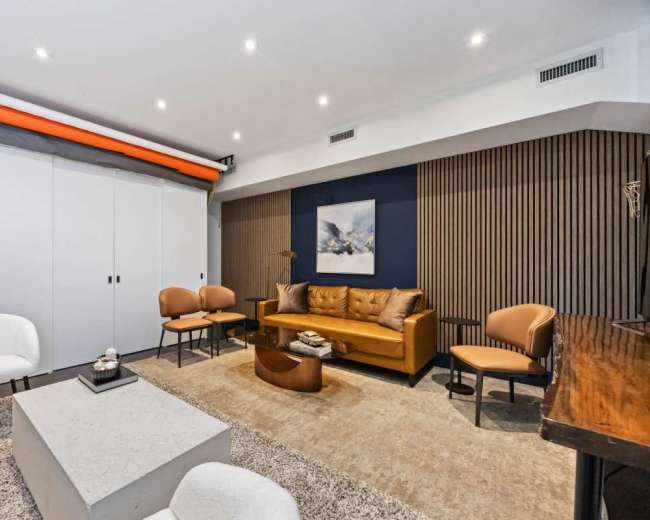 The image shows a modern living room with a brown leather sofa, three chairs, a coffee table, and a large area rug, all arranged around a minimalist design.
