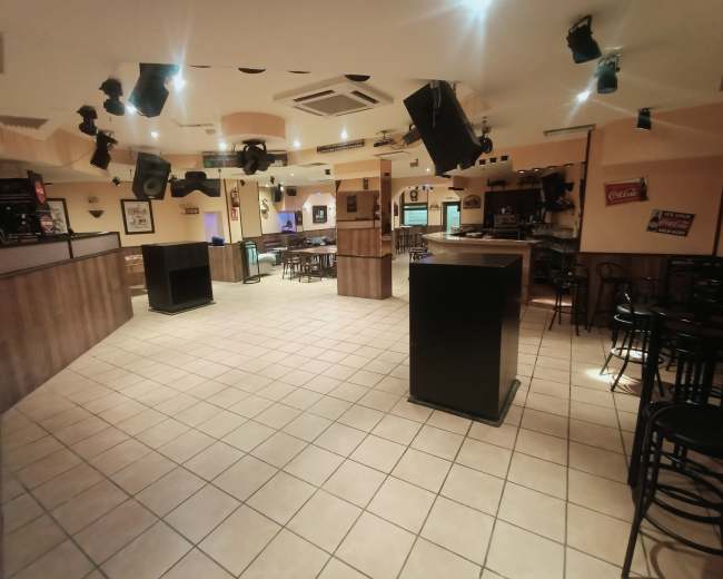 The image shows an empty bar interior with tiled flooring, a service area, and seating scattered throughout.