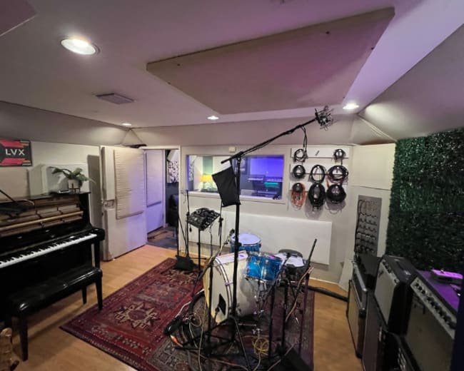 A music studio equipped with a drum set, a piano, and various musical equipment arranged around a patterned rug.