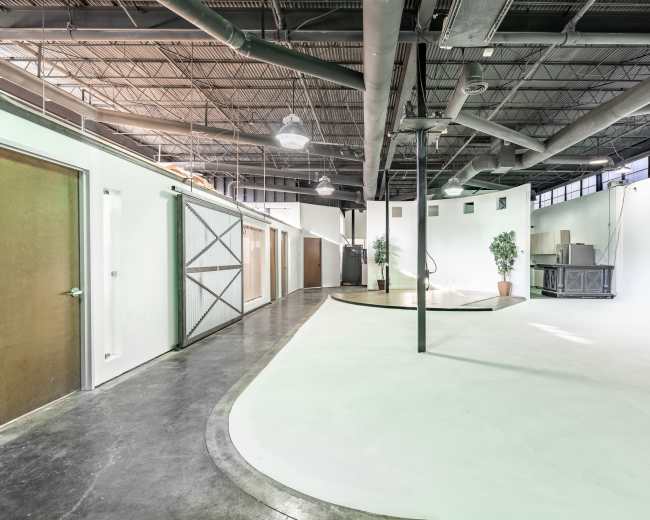The image shows an industrial-style interior space with several closed doors along the walls, a curved floor area, and potted plants.