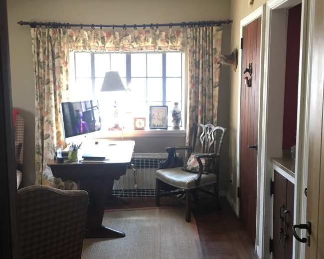 The image shows a well-lit room with a desk, a chair, floral curtains, and antlers mounted on the wall.