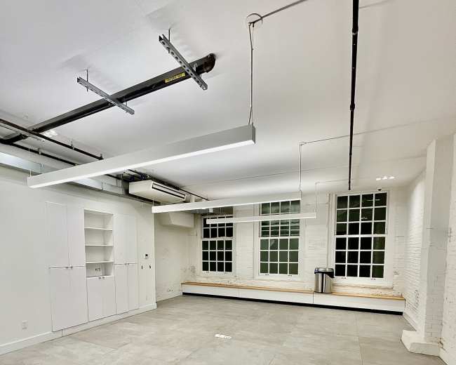 The image shows an empty and well-lit room with large windows, white walls, and gray tiled flooring.