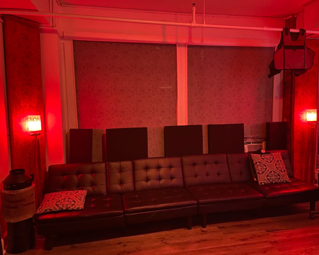 A dark room features a leather sectional sofa with decorative pillows, illuminated by red wall sconces.