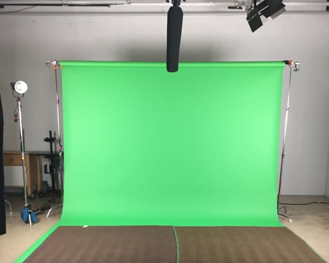 The image shows a green screen setup with lights and a microphone overhead in a studio space.