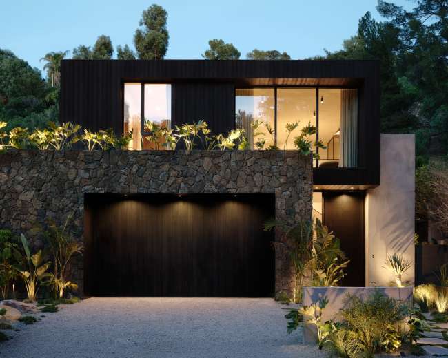 A modern house with a stone facade, large windows, and landscaping features is set against a backdrop of trees.