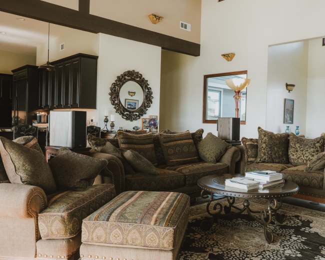 The image showcases a spacious living room with a large seating area featuring patterned sofas and a coffee table, accented by decor items and a mirror on the wall.