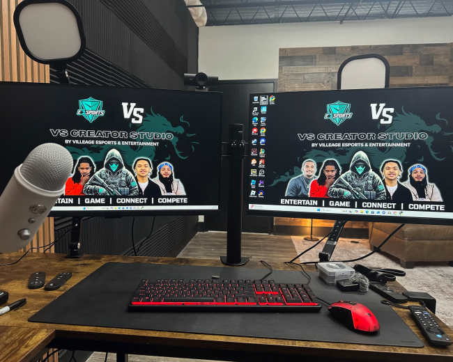 The image shows a gaming setup with two monitors displaying a banner for "VS Creator Studio" and a microphone on the desk.