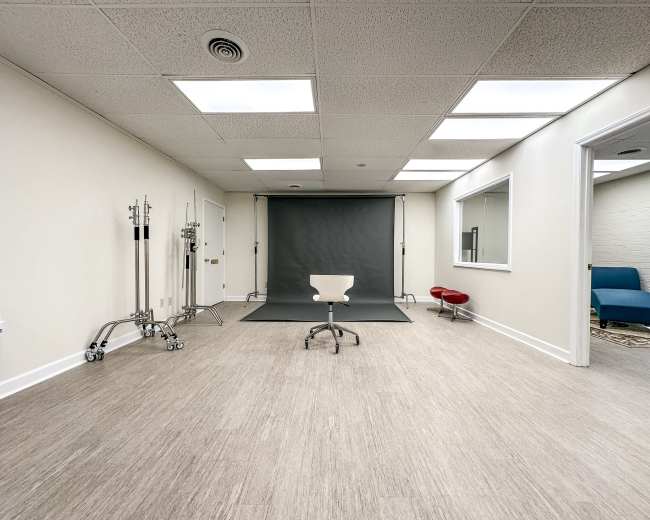 A spacious, empty photo studio featuring a chair in the center, a backdrop, and various studio equipment along the walls.