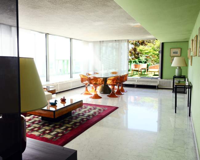 A modern living space features large windows, minimalist furniture, and a mix of green and neutral colors.