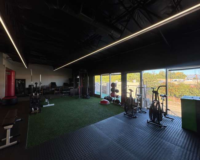 The image shows an indoor gym space with exercise equipment, including stationary bikes and weight benches, illuminated by overhead lights.