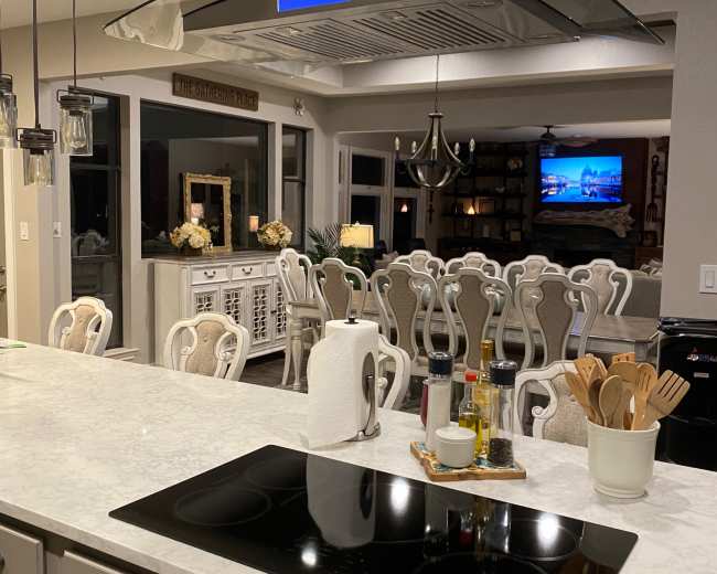 A modern kitchen with a marble countertop, a cooking range, and a visible dining area in the background.