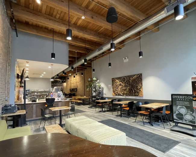 The image depicts the interior of a modern café with wooden beams, a bar area, and various seating arrangements.