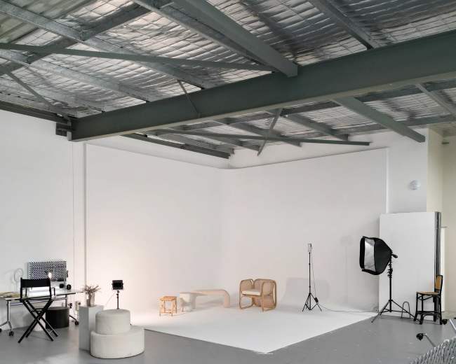The image shows a spacious photography studio featuring various pieces of furniture, a backdrop, and lighting equipment.
