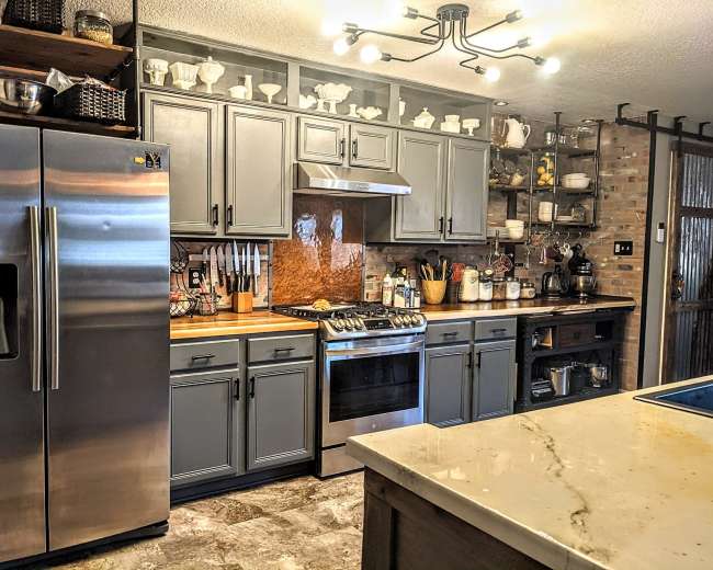 The image shows a modern kitchen featuring stainless steel appliances, gray cabinets, and a central island with a marble countertop.