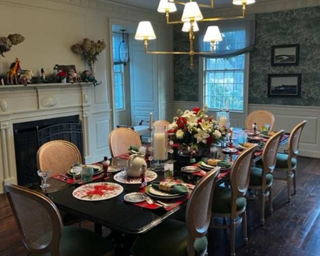 A large dining table is set for a meal, surrounded by chairs, with a floral centerpiece and a light fixture overhead in a well-decorated room.