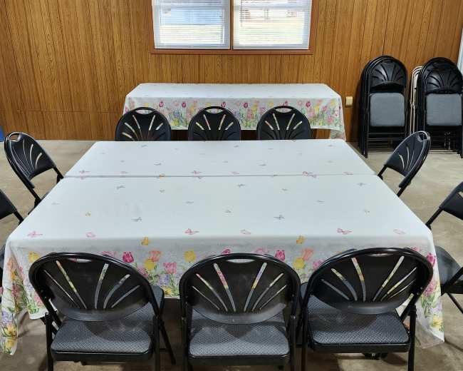 Several tables covered with floral tablecloths are set up in a room with black folding chairs arranged around them.