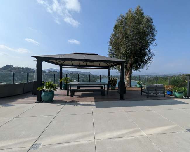 A gazebo with seating is situated on a concrete patio overlooking a scenic landscape.