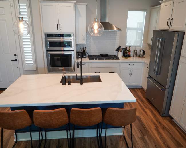 A modern kitchen featuring white cabinets, a large island with a sink, and four brown barstools.